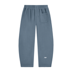 A pair of dusty slate blue sweatpants with an elastic waistband, a side pocket on the right leg, and a small white logo on the lower left leg, shown against a plain white background.