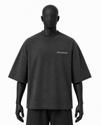 A dark charcoal gray oversized short-sleeve t-shirt displayed on a matte black mannequin against a plain white background. The shirt features a small white script logo on the left chest.