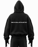A black pullover hoodie shown from the back on a mannequin or model, featuring the word 'REVIVALATHLETIC' printed in white across the upper back. The hoodie has a relaxed fit with a large hood and ribbed cuffs and hem.