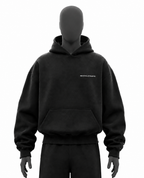A black pullover hoodie displayed on a matte black mannequin torso, featuring a small white text logo on the left chest that reads REVIVALATHLETIC. The hoodie has a front kangaroo pocket and ribbed cuffs and hem, shown against a solid white background.
