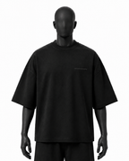 A black oversized short-sleeve t-shirt displayed on a matte black mannequin against a plain white background.
