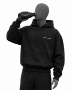 A black hoodie with a small white 'REVIVALATHLETIC' logo on the chest, shown on a gray mannequin wearing matching black sweatpants. The mannequin is holding a black bottle to its eye against a plain white background.